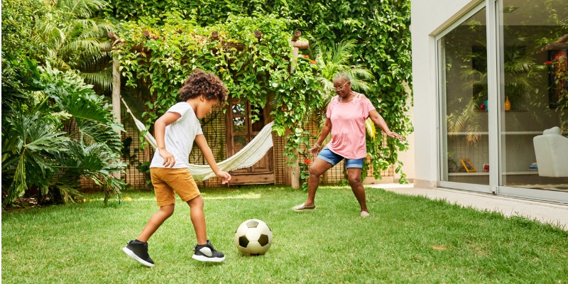 Young boy and grandmother playing soccer outside in the backyard.